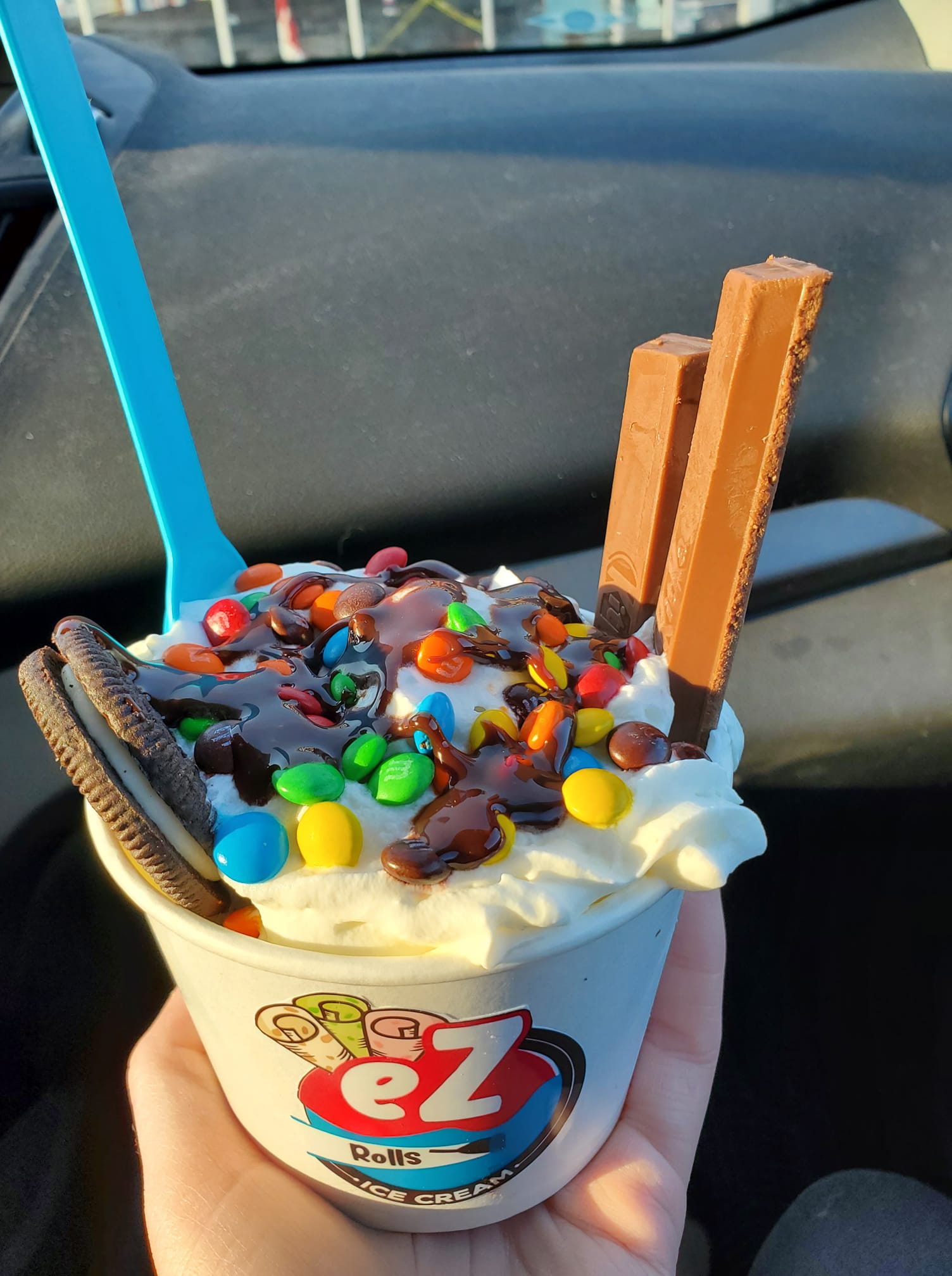 Loaded ice cream cup with M&Ms, Oreo cookie, wafer sticks, and chocolate drizzle